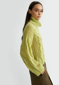 Maglione oversize in maglia a treccia di colore verde chiaro, con un colletto alto a coste e maniche ampie, caratterizzato da un motivo trasparente e testurizzato.