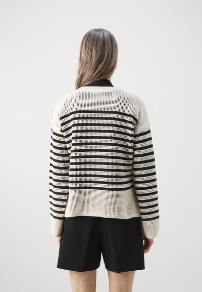 Cardigan en tricot beige avec des rayures horizontales noires. Présente une coupe décontractée, une texture à mailles ouvertes et un col noir contrastant.