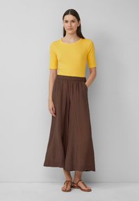 Haut à manches courtes rayé jaune associé à un pantalon large marron, doté d'une taille élastique et de poches latérales. Porté avec des sandales marron.