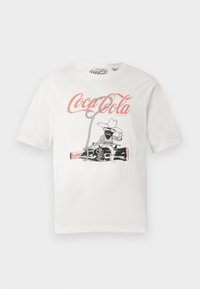 Valge puuvillane T-särk, millel on must ja roosa Coca-Cola graafika kauboikarakteriga ja nööriga, lühikeste varrukatega disain.
