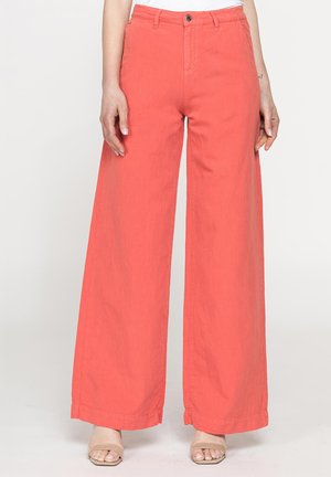 Pantaloni corallo a gamba larga con chiusura con bottone e cerniera, indossati con sandali beige a punta aperta, mostrati dalla vita ai piedi.