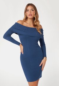 Blauwe off-shoulder jurk van gebreide stof, met parelaccenten op de halslijn en een gestructureerd patroon langs de voorkant. Slim fit, jurk tot op de knie.