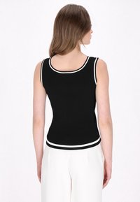 Schwarzes, geripptes Tanktop mit weißem Kontrastbesatz entlang des Ausschnitts und dem Saum. Hat eine figurnahe Silhouette und ärmelloses Design.