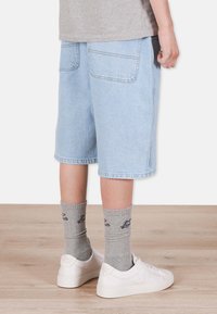 Ljust blå denimshorts med lös passform, knälång design och synliga bakfickor. I kombination med grå strumpor och vita sneakers.