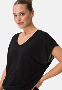Top nero a V in tessuto leggero e leggermente trasparente; presenta maniche corte e una vestibilità rilassata. Texture sottile, design minimalista.