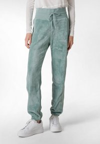 Fleece joggers i dæmpet grøn med snøre i taljen, elastiske manchetter og en blød tekstur, parret med hvide sneakers.