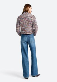 Mehrfarbiger Strickpullover mit strukturiertem Finish, kombiniert mit hellblauen, weit geschnittenen Jeans mit Gesäßtaschen.