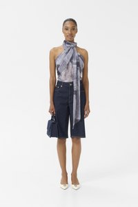 Denimshorts med høy midje og oppbrettede kanter, kombinert med en mønstrete halterneck-topp. Tilbehør inkluderer en liten håndveske og kremfargede hæler.
