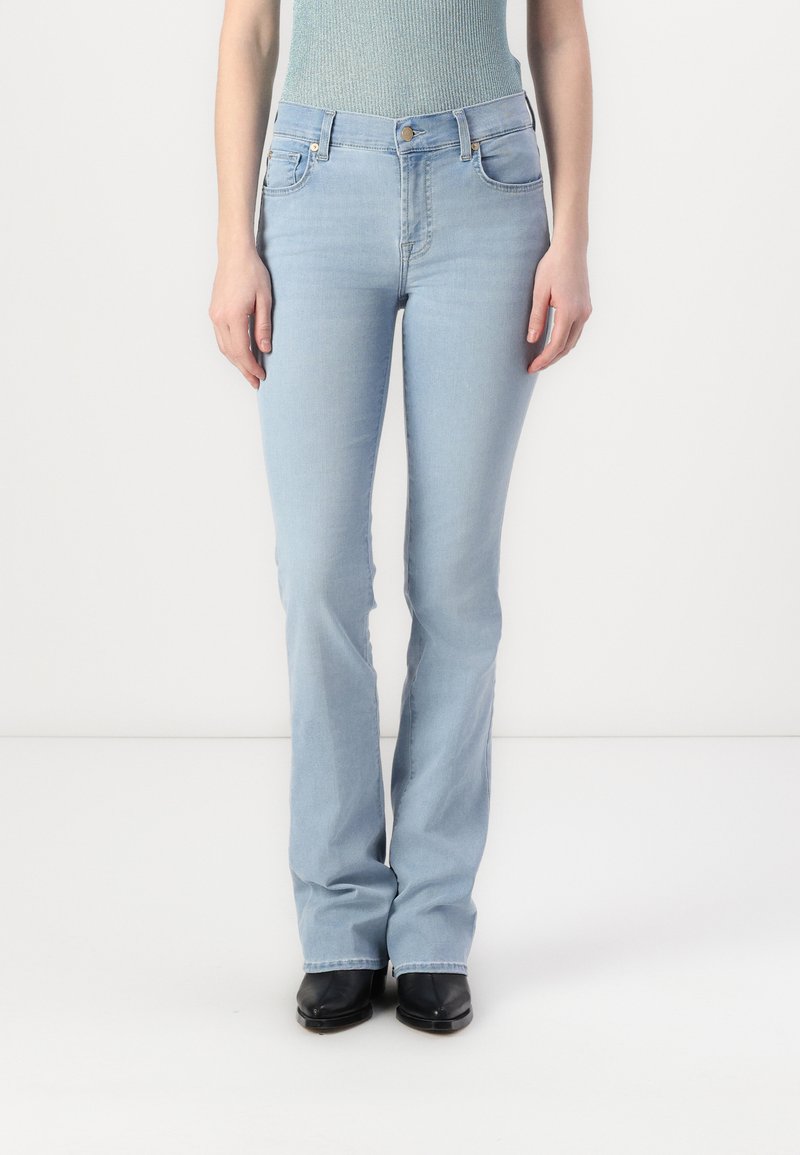 Blugi evazați de culoare albastru deschis, din denim, cu talie înaltă, cinci buzunare și un finisaj ușor decolorat. Stilizați cu cizme negre.