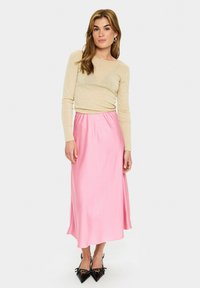 Lichtbeige langmouwtop gecombineerd met een vloeiende roze satijnen maxi rok. Zwarte puntige schoenen met delicate versieringen.