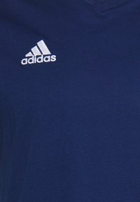 Tmavě modré tričko vyrobené z měkké látky, s výstřihem do V a bílým vyšitým logem Adidas nalevo na hrudi.