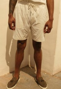 Pantaloni scurți de culoare crem, cu un model texturat de frunze, talie elastică cu șnur și buzunare laterale, purtați cu pantofi slip-on de culoare verde măslin.