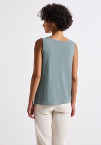 Ärm im tröja i mjukt teal-tyg med en avslappnad passform. Har en rund halslinning och en slät yta. Bärs med ljusa byxor.