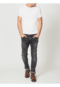 Camiseta blanca de manga corta, combinada con jeans gris oscuro y zapatos de cordones marrones. El conjunto presenta un ajuste relajado y un diseño clásico.