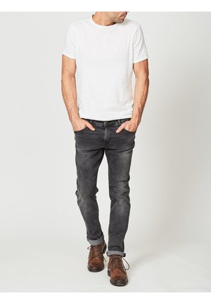 Tricou alb cu mânecă scurtă, asortat cu blugi de culoare gri închis și pantofi maro cu șireturi. Ținuta are un croi confortabil și un design clasic.