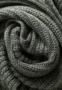 Acercamiento de una tela de lana gris oscuro tejida de manera compacta, con puntos texturizados visibles y capas dobladas.