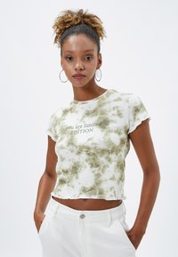 Korte mouwen cropped T-shirt in wit en groen tie-dye patroon, met de tekst "je bent een beperkte EDITIE" in het groen. Zachte stof met ruwe zoomranden.