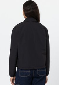 Giacca nera con colletto, polsini e orlo elasticizzati. Tessuto liscio, design casual, presenta una lavorazione minimale con una silhouette semplice.