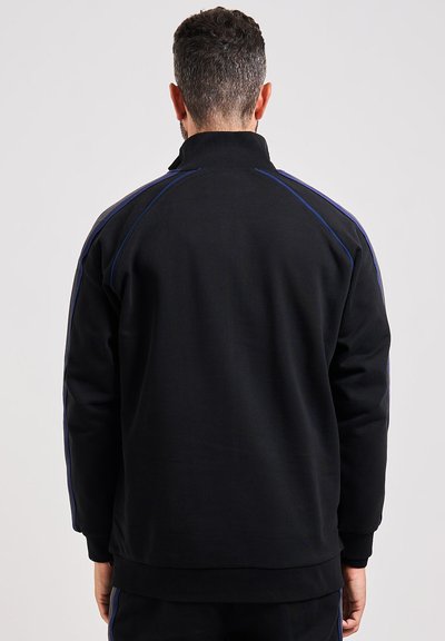 Felpa nera con colletto alto, dettagli blu lungo le spalle, polsini e orlo a coste, realizzata in tessuto morbido e con una texture liscia.