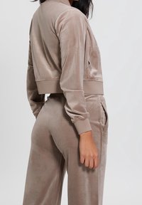 Velvet cropped jacket en bijpassende broek in licht taupe. Heeft een zachte textuur, zijzakken en ribgebreide manchetten, en biedt een relaxte pasvorm.