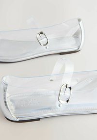 Läpinäkyvät PVC-lapikkaat, joissa on hopeinen koristerintaneula, minimalistisella muotoilulla ja sileällä pinnalla. Sopivat arkikäyttöön.