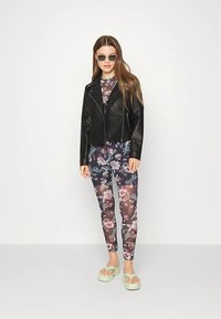 Casaco curto de couro sintético preto sobre um body floral de manga comprida e leggings, com sandálias plataforma verde claro e óculos de sol.