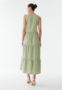 Maxi-jurk in lichtgroen, mouwloos ontwerp met gelaagde rok. Gladde stof en zichtbare naden, gecombineerd met sandalen met hak.