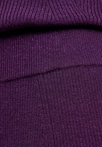 Paarse gebreide stof met een geribbelde textuur en metallic draden die erdoorheen zijn geweven, wat een schitterend uiterlijk creëert.