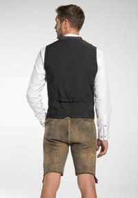 Schwarze Stoffweste mit gerafftem Rücken, kombiniert mit hellbraunen Lederhosen, die mit Knopfakzenten und einer glatten Textur versehen sind.