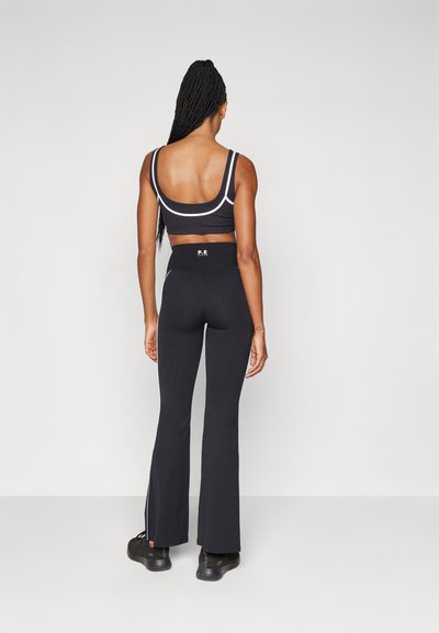 Black athletic wear featuring a fitted crop top with wide straps and high-waisted flared pants, accented with side slits and a logo.
