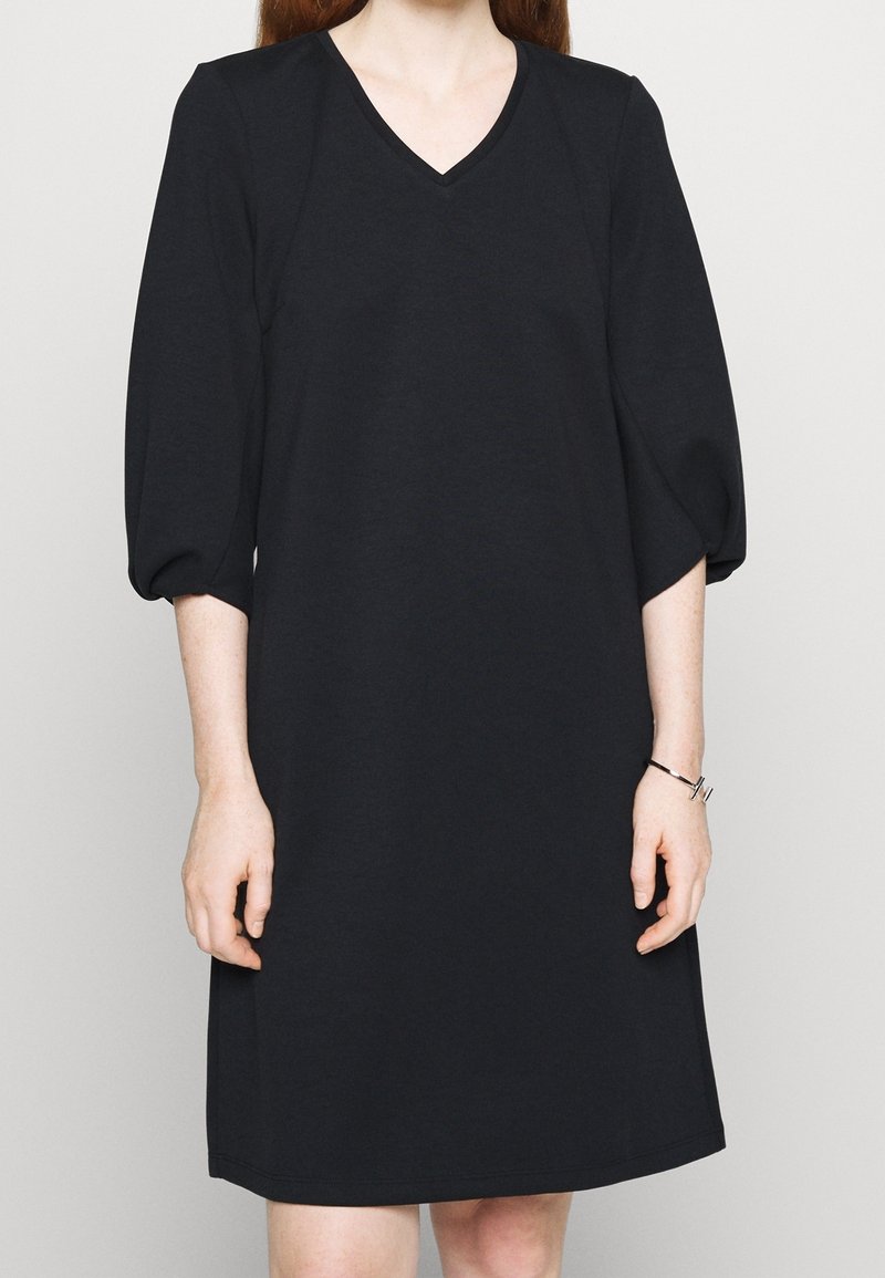 Robe noire, mi-longue, avec un décolleté en V et des manches bouffantes trois-quarts. Fabriquée à partir d'un tissu doux et texturé avec une coupe décontractée.