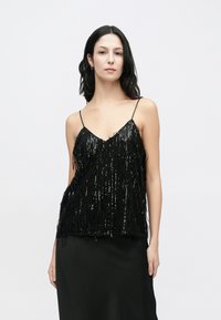 Black sequin top with fringe detailing, featuring thin straps and a V-neck design. Smooth texture with a relaxed fit, paired with a black skirt.