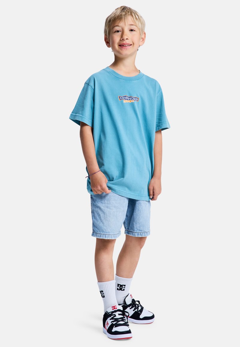 Svetlomodré bavlnené tričko s krátkymi rukávmi a logom, skombinované s riflovými krátkymi nohavicami. Doplnok biele ponožky a čierno/červené tenisky.