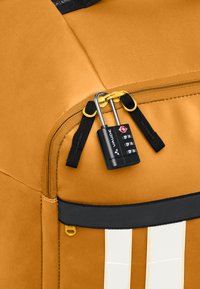 Borsa di stoffa gialla con una cerniera nera dotata di lucchetto. Include spallacci neri e strisce bianche a contrasto, che evidenziano il suo design strutturato.