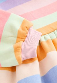 Close-up af en ærme på et stykke tøj med lyserød ribbet manchet og stof med horisontale pastelfarvede striber i orange, grøn, pink, lilla og blå.