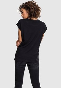 Sort T-shirt lavet af blødt bomuld, med korte oprullede ærmer og en afslappet pasform, parret med mørke skinny jeans.