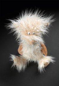 Fluffy plush toy with a light beige, shaggy fur texture, blue plastic eyes, and soft brown ears, featuring a rounded body and limbs.