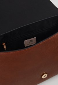 Hnědá kožená kabelka s texturovaným povrchem, s černou látkovou vnitřní částí, zipovou kapsou a zlatým kovovým detaily.