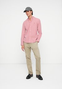 Red and white striped button-up shirt paired with beige trousers and black loafers. A gray cap completes the outfit.