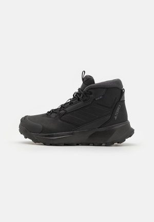 Czarne buty trekkingowe z wysoką kostką, syntetyczna cholewka, fakturowana powierzchnia, wzmocniony nos i szorstka podeszwa zapewniająca przyczepność.