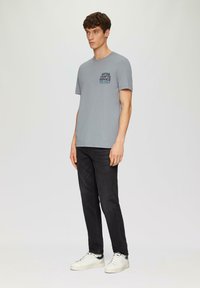 Grijze T-shirt met korte mouwen en een grafisch voorzakje. Gecombineerd met donkere jeans en witte sneakers. Eenvoudig, casual ontwerp en pasvorm.