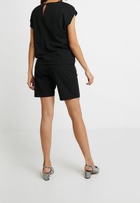 Black short-sleeve top with back keyhole detail, paired with black shorts. Worn with patterned high-heeled sandals.