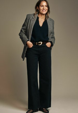 Tjekket blazer i grå og sort, båret over en mørk skjorte med knapper, parret med marineblå vide bukser og et brunt bælte med en sølvspænde.