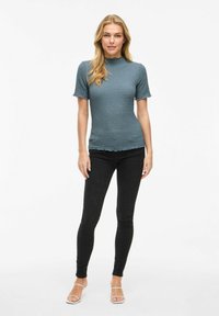 Top texturizzato color teal con maniche corte e orlo scallop, abbinato a jeans skinny neri e sandali bianchi con cinturini.