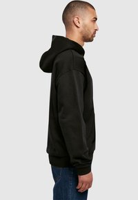Sort hættetrøje med kengurulomme, ribbede manchetter og kant, afslappet pasform, blød tekstur og stor hætte. Båret med blå jeans.