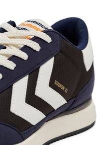 Marineblå og brune sneakers lavet af teksturerede materialer, med hvide chevron-detaljer og "STADION 23" printet i guld på siden.