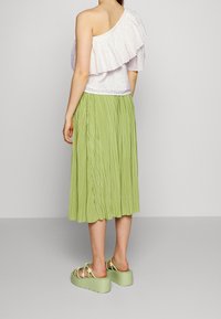 Blusa bianca asimmetrica con dettagli a volant, abbinata a una gonna midi verde plissè e sandali chunky verde chiaro con decorazioni floreali.