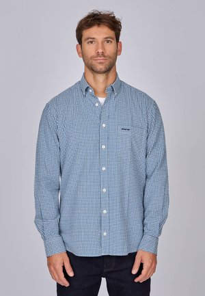 Chemise à manches longues à carreaux bleu et blanc avec col boutonné, dotée d'une poche sur la poitrine gauche et d'une coupe décontractée. Texture en tissu de coton.