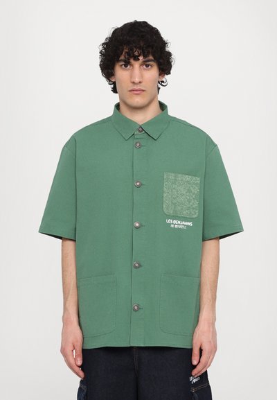 Zeleno kratkodlako srajco iz bombaža z teksturirano žepom in sprednjimi gumbi. Ima dva sprednja žepa in tiskano blagovno znamko.