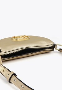 Borsa dorata con apertura con zip, dotata di un logo prominente sul fronte e una tracolla regolabile. Lo sfondo è bianco semplice.